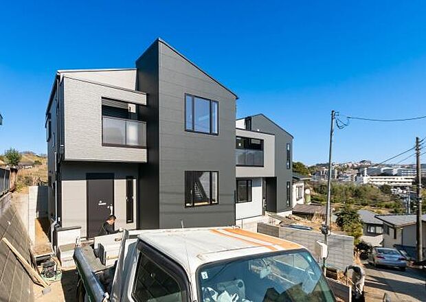 ゆとりあるカースペースと、日当たりの良い南面の庭を確保した配置計画。白とグレーを基調としたモダンな外観デザインが、青空に映える存在感のある住まいです。