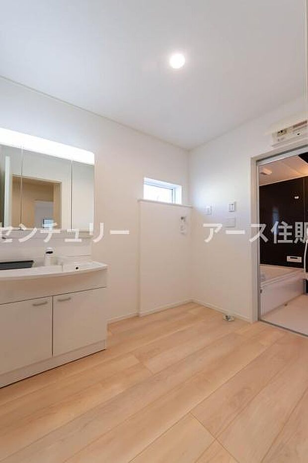 白を基調とした清潔感あふれる洗面室。浴室のモダンなアクセントウォールが、日々の疲れを癒やす上質な空間を演出します。