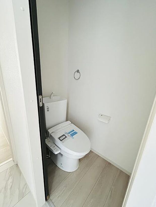 清潔感のあるトイレ空間です。シンプルな内装でお手入れもしやすい仕様です。使い勝手を考えた設備が整っています。壁や床も落ち着いた色合いでまとめられています。