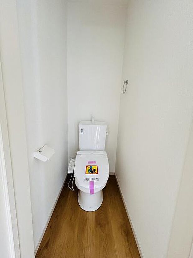 シンプルなデザインで清潔感のあるトイレです。床材と壁の色合いが調和し落ち着いた空間を演出しています。ペーパーホルダーやタオル掛けが設置されていて使いやすさにも配慮されています。