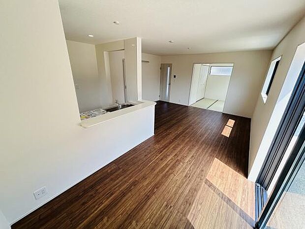 リビングは大きな窓から自然光がたっぷりと差し込み室内が明るく感じられます。床は落ち着いた色合いでさまざまなインテリアに調和しやすいです。キッチンとのつながりもよく開放感のある空間になっています。