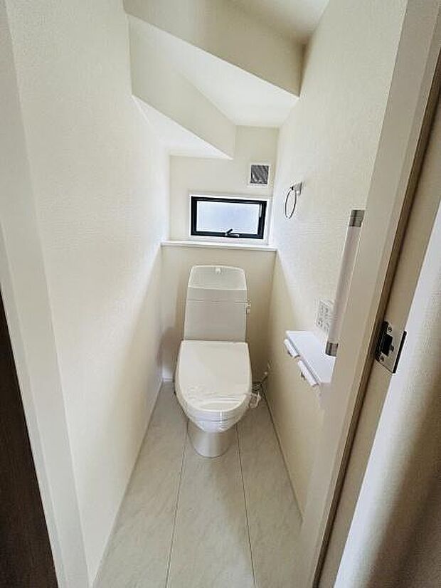 明るい窓付きで自然な光が差し込むトイレです。清潔感のある内装で使い勝手の良い設計です。手すりやペーパーホルダーも設置されており日常的に使いやすい空間です。
