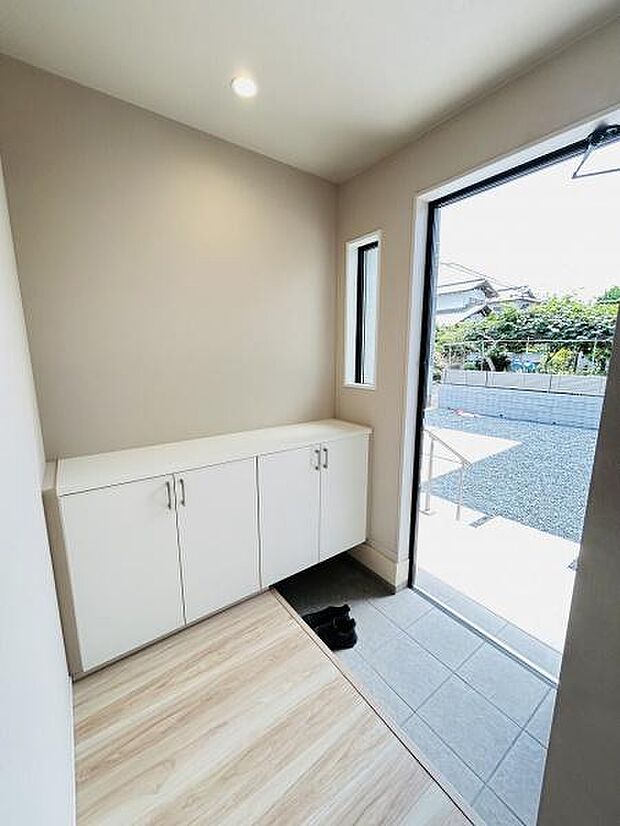 玄関には大きめの収納が備わっておりスッキリとした印象です。窓からは外の明るさが差し込み開放感があります。床の色合いも優しく全体的に明るい空間となっています。シンプルな設計で手入れもしやすい玄関です。