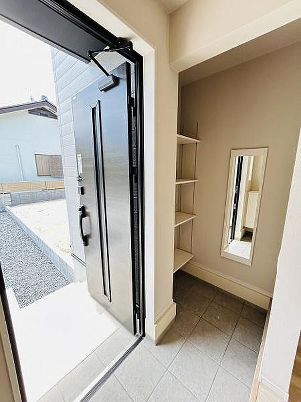 玄関は明るい印象で清潔感があります。収納棚が設置されており整理がしやすい空間です。全身鏡が備え付けられているため外出前の身だしなみチェックに便利です。広さもゆとりが感じられます。