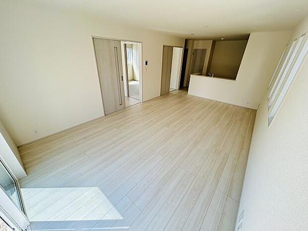 明るい光が差し込む広々としたリビングです。淡い色合いのフローリングが空間をすっきりと感じさせます。窓からの採光で室内がより広く見えます。キッチンとの繋がりも便利です。収納スペースも確保されています。