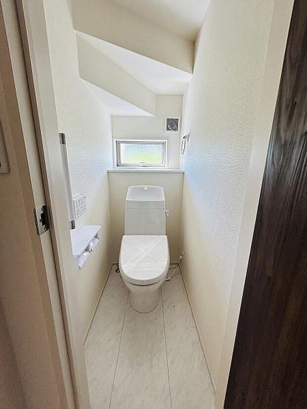 窓から自然光が差し込む明るいトイレです。シンプルな内装で清潔感があります。収納しやすいスペースがあり使い勝手の良い形状です。ゆったりとしたスペースを確保しています。ペーパーホルダーも設置されています。