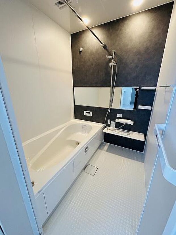 落ち着いた色合いの壁面がアクセントになったバスルームです。大きなミラーが空間を広く見せます。浴槽はゆったりとしたサイズ感です。シャワーや洗面スペースもすっきりまとまっています。