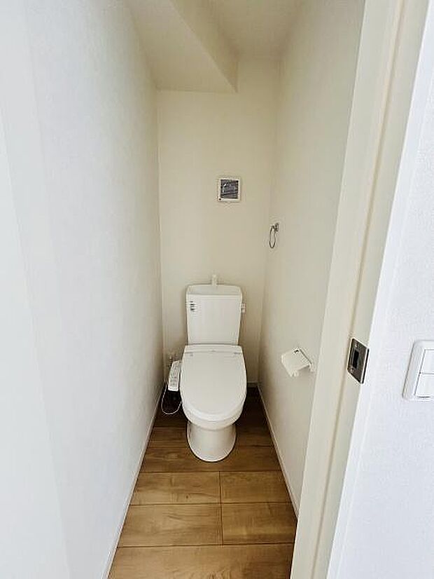 明るい色合いの壁と木目調の床が清潔感を演出しています。手洗い付きトイレで日常使いに便利です。空間がすっきりとしておりお手入れもしやすい仕様です。ペーパーホルダーやタオルリングも設置されています。