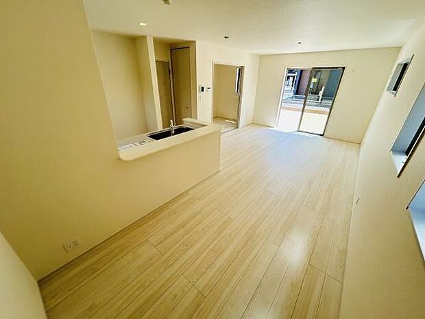 リビングは明るい色合いのフローリングが印象的です。大きな窓からしっかりと陽射しが入ります。キッチンとのつながりも良好な空間設計です。ゆとりある広さが魅力的です。窓の配置も工夫されています。