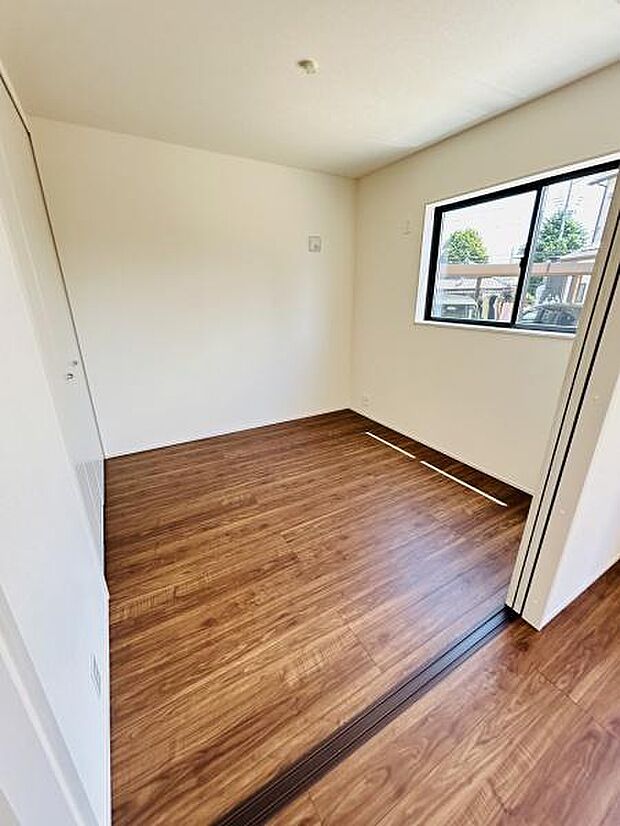 明るい光が差し込む洋室です。窓からの景色が楽しめる点も魅力です。シンプルな内装で様々なインテリアに合わせやすい空間です。木目調フローリングが室内に温かみを与えます。清潔感のある仕上がりです。