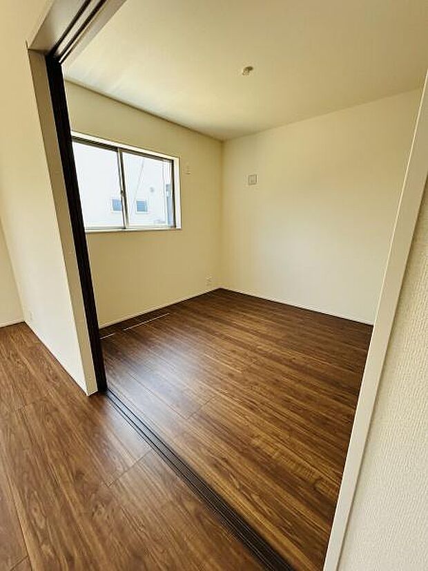 明るい窓から自然光が広がる洋室です。落ち着いた色合いのフローリングが空間を引き締めています。シンプルな内装で家具のレイアウトがしやすい洋室です。引き戸を使った間取りもポイントです。