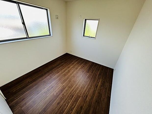 シンプルな白い壁と濃い木目調の床が特徴的な洋室です。二面採光で自然光が室内にしっかり入ります。コンパクトながらも居心地の良い空間となっています。無駄のないデザインが魅力的です。