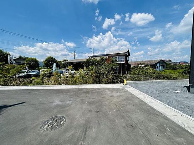 前面道路が広々とした印象の現地写真です。周囲には植栽や住宅があり落ち着いた雰囲気が感じられます。空が抜けていて開放感があります。舗装された道路が整っています。車の出入りもしやすそうです。