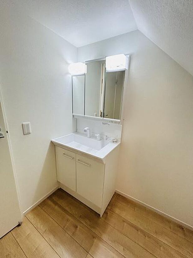 すっきりとしたデザインの洗面台が特徴です。ミラーキャビネットが備わっており小物をしっかり収納できます。照明が手元を明るく照らしてくれます。木目調の床が空間を引き締めています。