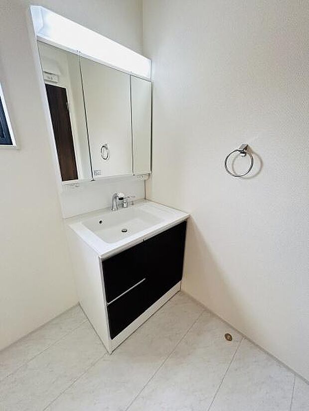 洗面台はシンプルなデザインで使いやすさを重視しています。収納スペースも十分に確保されており日々の身支度に便利です。明るい空間で清潔感があります。壁面にはタオルリングが設置されています。