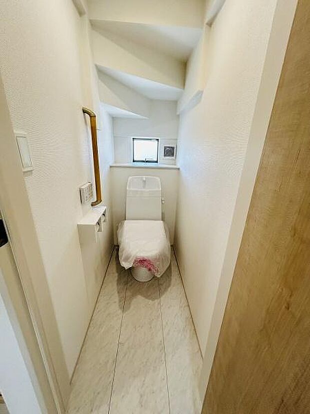 窓付きで換気がしやすいトイレです。シンプルな内装で清潔感があります。コンパクトな空間を有効に活用しています。小物を置ける棚も設けられています。明るい雰囲気のトイレです。