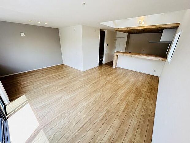 大きな窓から光が差し込むリビングです。ナチュラルな木目調の床が空間を明るく演出します。奥にはカウンターキッチンがありシンプルな内装が魅力的です。落ち着いたカラーの壁面がアクセントになっています。