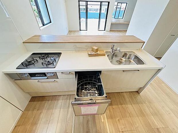 キッチンはシンプルで清潔感のあるデザインです。食器洗い乾燥機が設置されており日々の家事をサポートします。カウンター下には収納スペースも確保されています。窓が複数あり明るい印象が特徴的です。