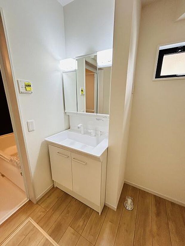 清潔感のある白を基調とした洗面台が設置されています。鏡面収納付きで空間をすっきり見せます。隣接する浴室との動線も良好です。窓があり採光も確保されています。使い勝手の良い洗面スペースです。