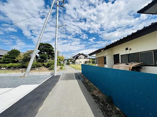前面道路は車両の通行がしやすい広さです。周囲には住宅が立ち並び落ち着いた雰囲気が広がっています。道路沿いには緑も多く季節の移り変わりを感じられる環境です。現地の空は開けており明るい印象です。