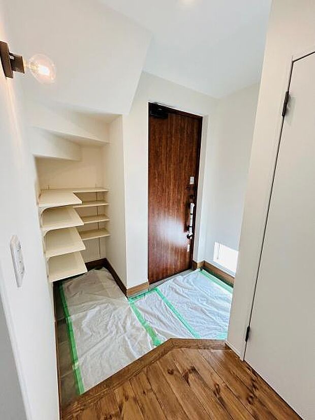 白を基調とした明るい玄関は清潔感が感じられます。木目のドアが空間に温もりをプラスしています。シンプルな棚があり使いやすい印象です。天井が高く開放的な雰囲気です。