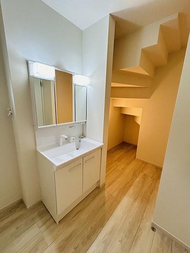 洗練されたデザインの洗面台が設置されています。収納スペースもあり使い勝手に配慮されています。照明付きミラーが明るさを確保します。階段下スペースが有効活用されています。