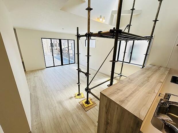 大きな窓から光が差し込むリビングです。ナチュラルな色合いのフローリングが広がります。キッチンからリビング全体を見渡すことができます。天井が高く開放感があります。