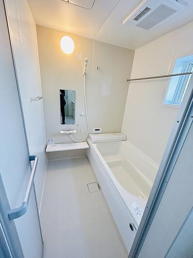 清潔感のある明るいバスルームです。鏡や手すりが設置されており使いやすい仕様です。浴室乾燥用のバーも備えられています。通風窓が付いており換気にも配慮されています。