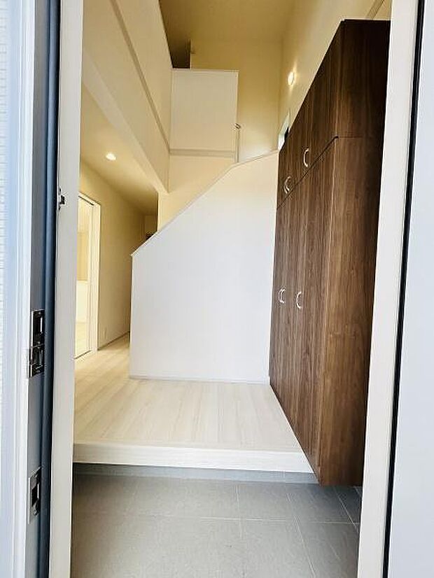 玄関スペースが広々としており開放感があります。木目調の収納が印象的で整理整頓しやすい設計です。床の色合いが明るく全体的に清潔感のある空間になっています。照明も程よく配置されスッキリとした印象です。