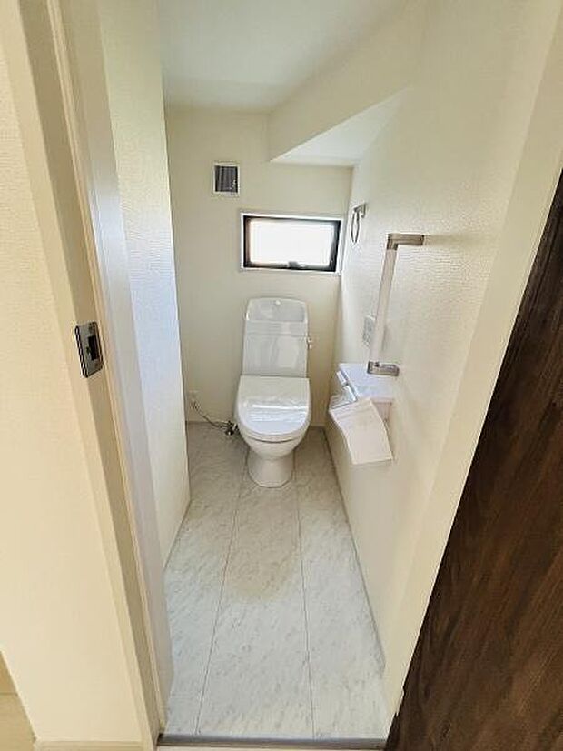 明るい光が差し込む窓付きのトイレです。壁面に手すりやペーパーホルダーがあり便利に使えます。清潔感のある内装で清掃もしやすい設計です。シンプルなレイアウトで使いやすい空間です。
