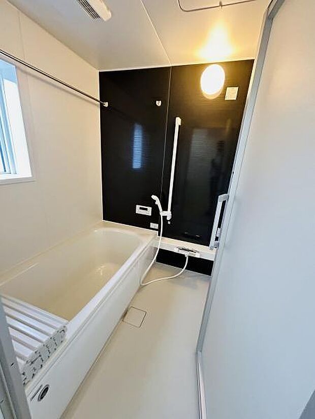 清潔感のあるバスルームが印象的です。モノトーンの壁面が空間を引き締めています。浴室乾燥機付きで快適にご利用いただけます。手すりも備え付けられており安心です。換気窓もあり湿気対策も考慮されています。