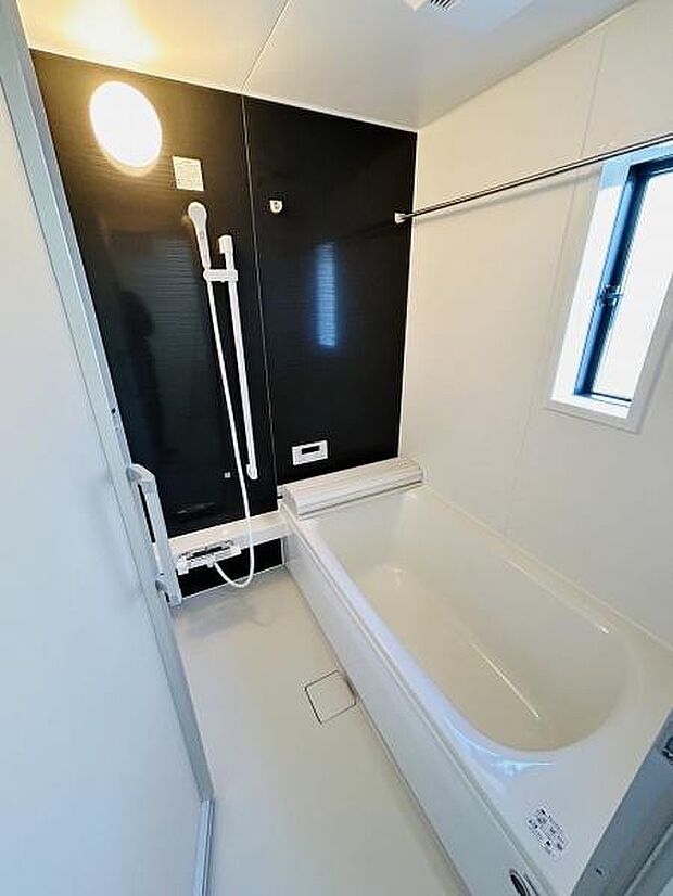 明るい照明がバスルーム全体を照らしています。シンプルな内装で清潔感があります。窓があるため換気もしやすいです。シャワー設備が備え付けられています。浴槽も十分な広さがあります。