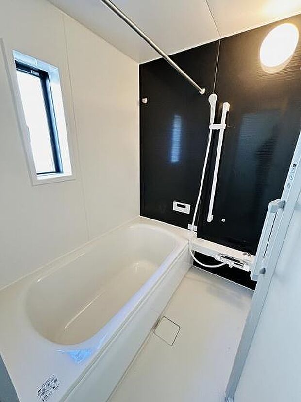 バスルームは白と黒を基調としたすっきりとしたデザインです。大きな浴槽がゆったりとしています。窓からの採光で明るさを感じます。手すり付きで安心して使用できます。清潔感のある空間が広がっています。