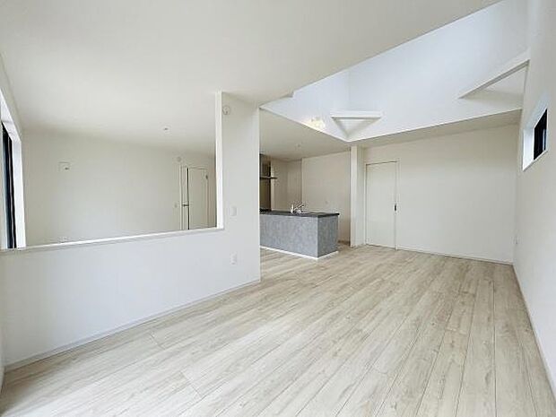 明るい色合いのフローリングが広がるリビングです。天井が高く開放感のある空間が特徴です。大きな窓から自然光が差し込み室内が明るく感じられます。キッチンとリビングが一体となったレイアウトです。