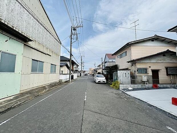 前面道路は広めで車の通行がしやすい印象です。周囲には住宅や工場が並び落ち着いた雰囲気が感じられます。道路沿いには電柱や配線も整然と配置されています。現地の状況やアクセスも写真からご確認いただけます。