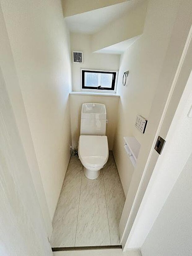 清潔感のあるシンプルなデザインのトイレです。コンパクトながらも窓が設けられているので換気も安心です。収納やペーパーホルダーも設置されています。明るい光が差し込む空間です。
