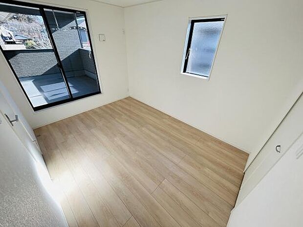 明るい日差しが差し込む子供部屋です。大きめの窓とバルコニーへのアクセスが特徴的です。ナチュラルな床材で清潔感があります。シンプルな内装で家具の配置がしやすい空間です。収納スペースも備えられています。