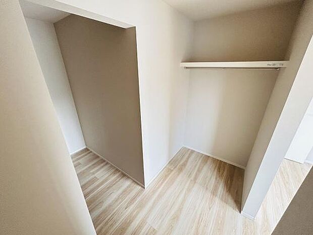 ゆったりとしたスペースが確保された収納エリアです。壁面にはハンガーパイプが設置され衣類の整理が便利です。床は明るい色合いで室内を広く感じさせます。仕切りがあり収納物の分類もしやすいレイアウトです。