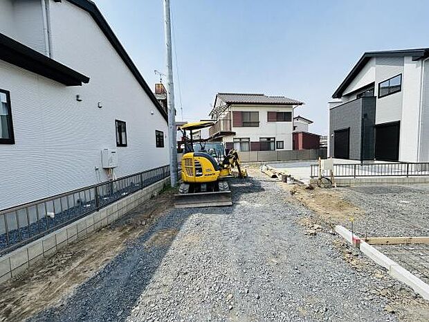 現地の様子が分かりやすい写真です。前面道路が広く周囲の住宅との距離感も確認できます。建築作業の進捗状況もご覧いただけます。整備された敷地内の状態が伝わります。