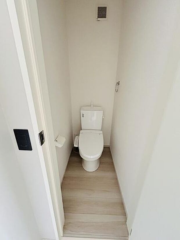 清潔感のあるシンプルなトイレ空間です。換気設備が備わっています。落ち着いた色合いの床材が採用されています。手洗い付きタイプです。ペーパーホルダーも設置済みです。