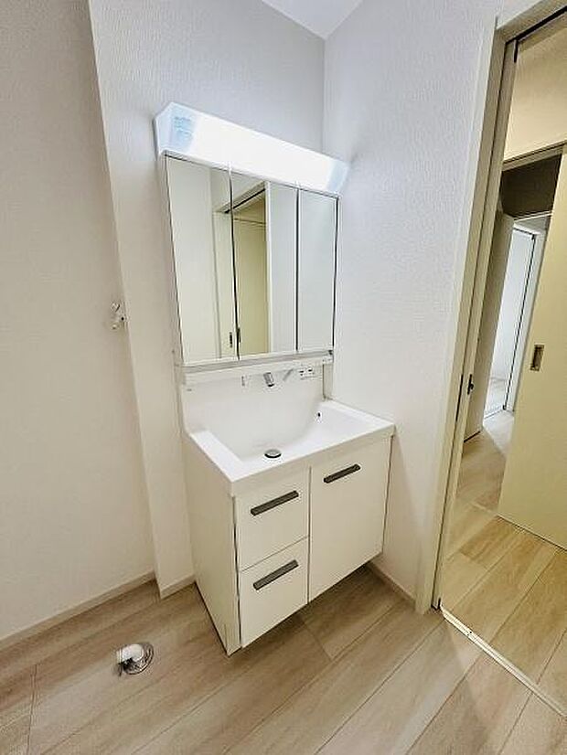 清潔感のある洗面台が設置されています。鏡面収納が便利に使えます。シンプルなデザインで空間が広く感じられます。明るい照明で身支度にも適しています。床色と調和の取れた洗面所です。