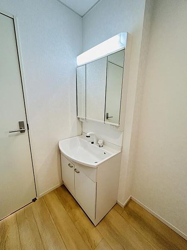 シンプルで清潔感のある洗面台が設置されています。収納スペースも備わっているため日用品の整理も可能です。明るい照明付きで使い勝手にも配慮されています。木目調の床が空間に温かみをプラスしています。