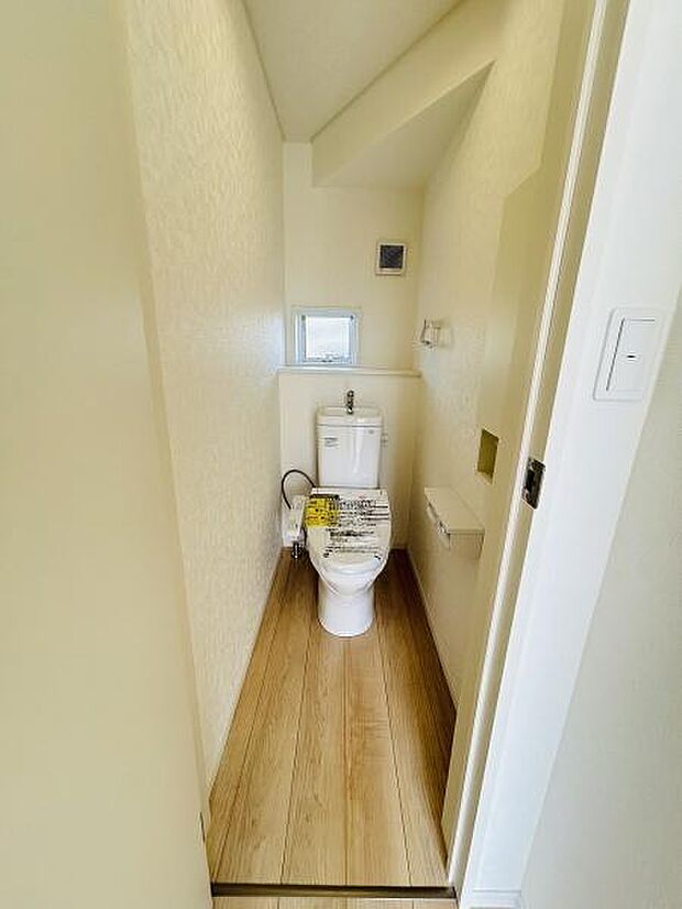 明るい色合いの内装で圧迫感を感じにくいトイレです。小窓付きで換気にも配慮されています。シンプルなデザインで清掃もしやすいレイアウトです。温かみのあるフローリング調の床が印象的です。
