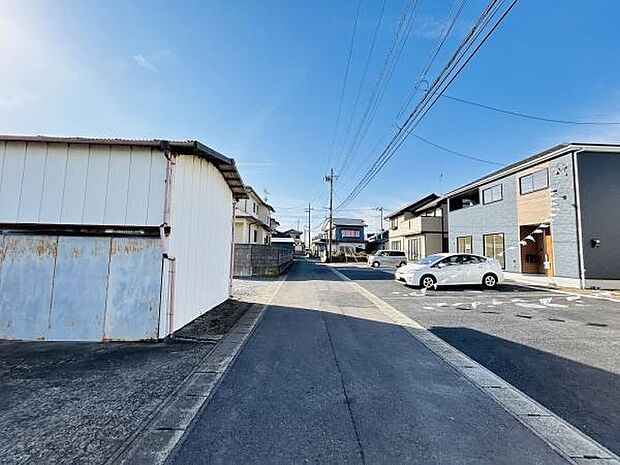 広々とした前面道路が印象的な現地写真です。車の出し入れもスムーズに行えます。周囲には新しい住宅が並び落ち着いた雰囲気が感じられます。青空が広がる気持ちの良いロケーションです。