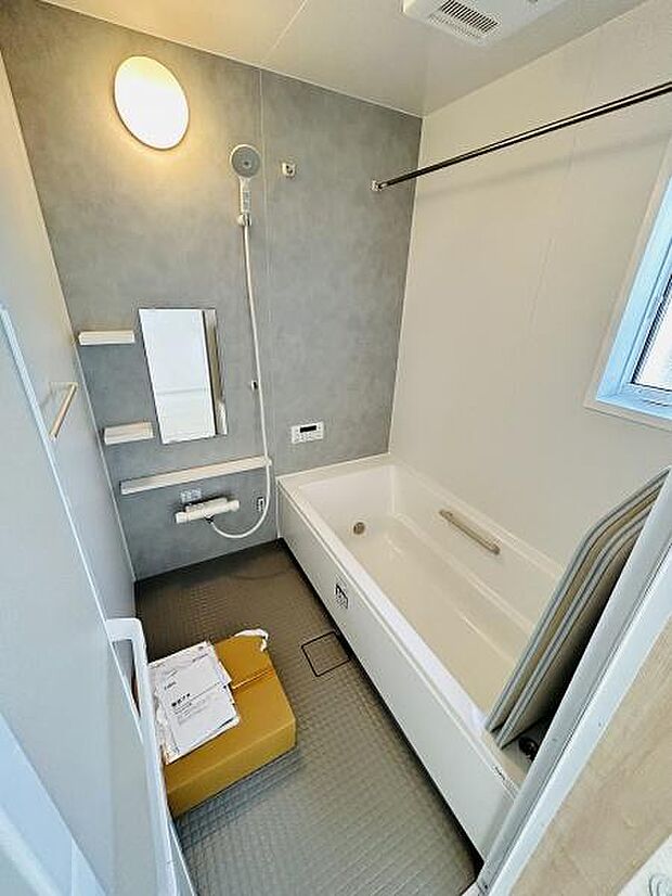 シャワーヘッドと手すりが設置されており使い勝手の良いバスルームです。窓があり換気にも配慮されています。壁面のアクセントカラーが落ち着いた印象です。収納棚やミラーも備え付けられています。