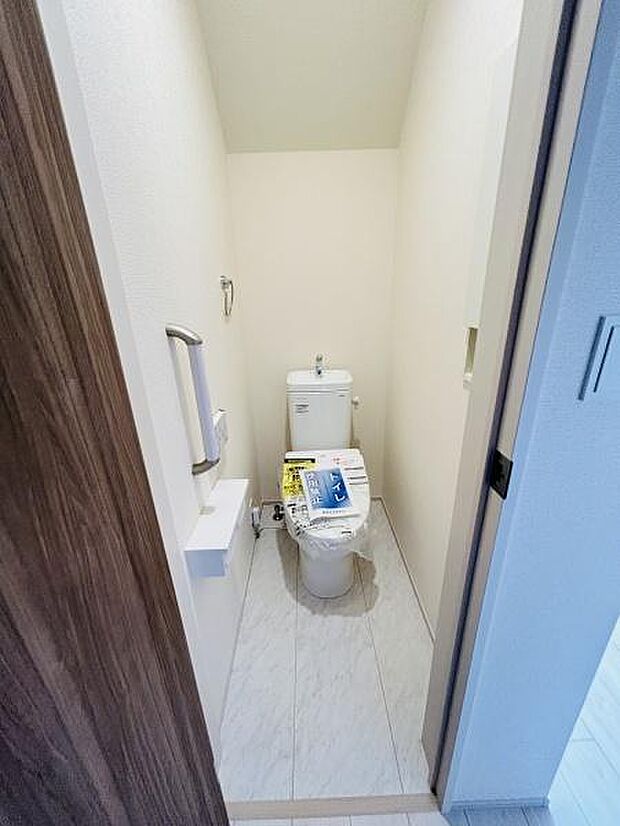シンプルで無駄のないデザインのトイレスペースです。壁の色合いが落ち着いた印象を与えます。ペーパーホルダーや手すりも設置されています。床材も明るくお掃除しやすい仕様です。