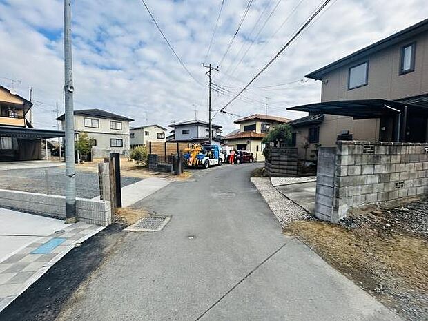 前面道路が整備されており周辺には住宅が立ち並んでいます。電柱や配線もきちんと管理されておりすっきりとした印象です。現地の様子がわかりやすい写真になっています。周囲には車の通行が見受けられます。