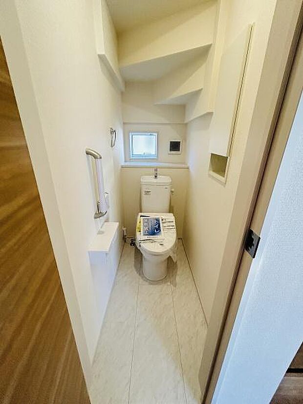 明るい印象のトイレです。コンパクトな空間ながら手すりが設置されています。窓があり換気や採光に配慮されています。壁面の収納スペースも便利です。清潔感のある内装です。