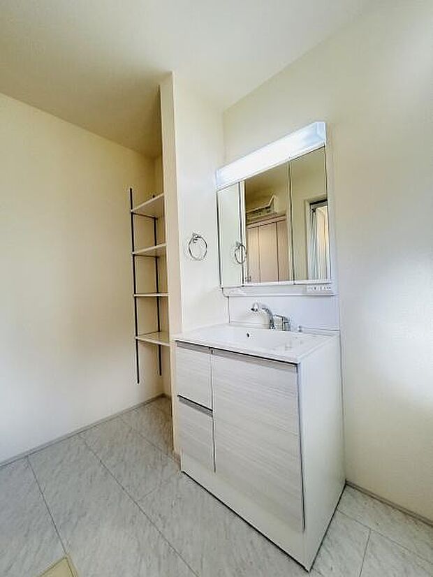 洗面台はシンプルなデザインで清潔感があります。大きな鏡が設置されており明るい印象です。隣にオープン棚があるため小物やタオルの収納にも便利です。ゆったりとした空間が確保されています。