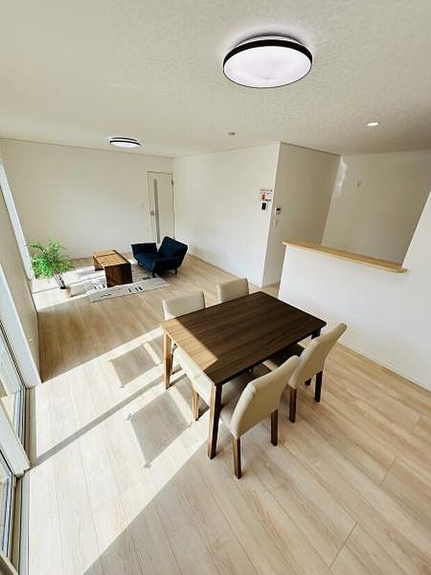 大きな窓から光がしっかりと入り明るく開放感のあるリビングです。ナチュラルな木目調の床が全体の印象を柔らかくします。ダイニングスペースとリビングスペースがゆるやかにつながっています。